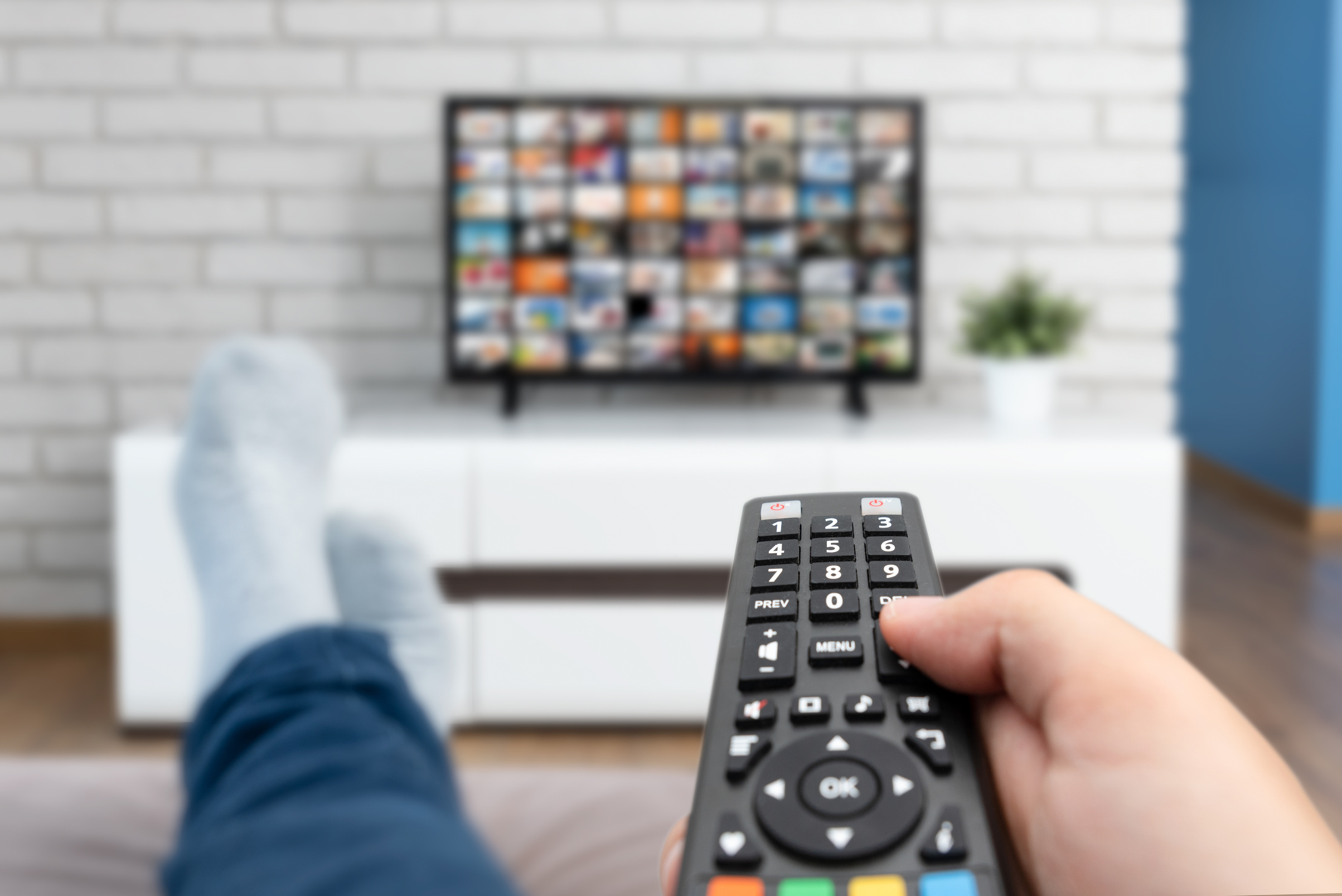 Hand Using Remote Control for TV with Legs on Table